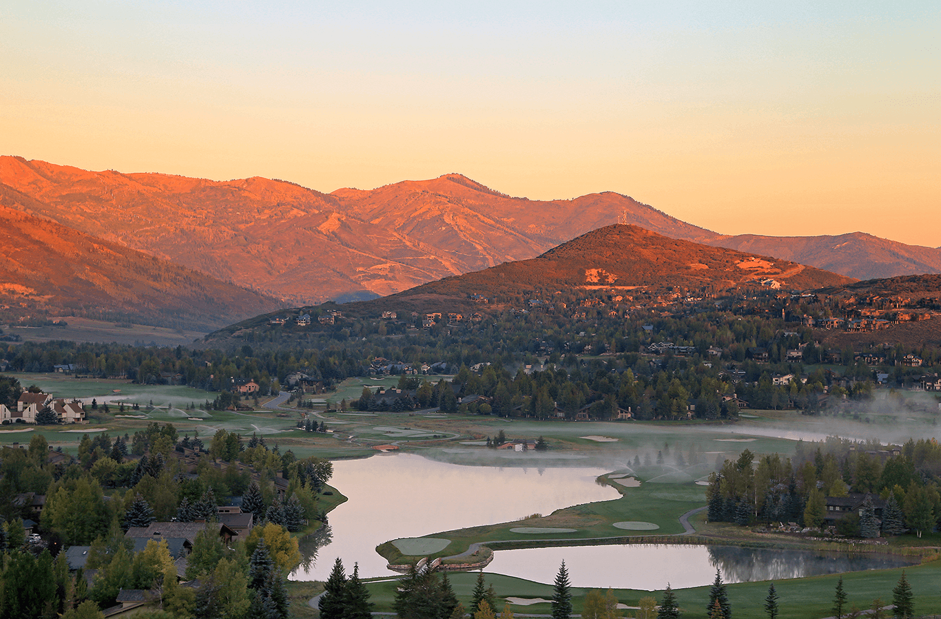 a scenic view of a golf course with a lake and mountains in the background in Park Meadows